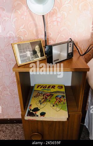 Ein alter Nachttisch mit Familienfotos, ein altes Transistor-Radio und eine Kopie des Tigers jährlich aus dem Jahr 1959. Stockfoto