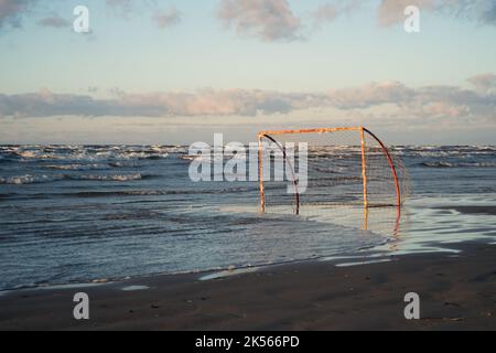 Im warmen Abendlicht an der ostseeküste umgeben sich anbrechende Wellen um ein Fußballtor am Strand Stockfoto