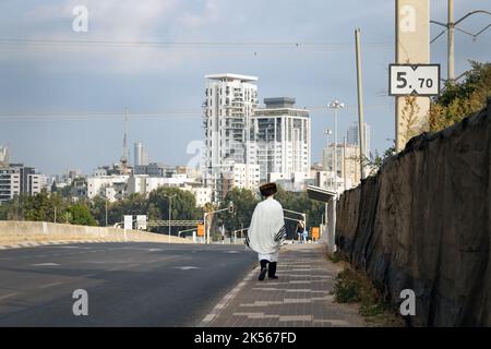 orthodoxer jüdischer Mann in einem Gebetstuch, der in der leeren Straße auf Yom Kippur spazierend ist. Stockfoto