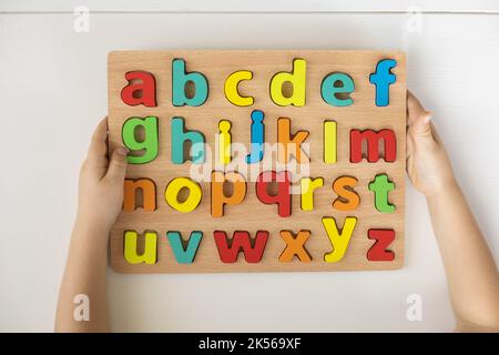 Kindliche Hände halten Alphabet Holzbrett mit farbigen Schriftbuchstaben in Zellen Nahaufnahme isoliert Stockfoto