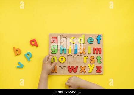 Kindliche Hände halten Alphabet Holzbrett mit farbigen Schriftbuchstaben in Zellen Nahaufnahme isoliert Stockfoto