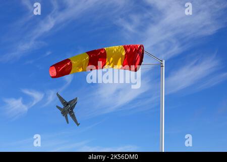 Gelb und rot gestreifte Windsocke oder Windkegel gegen den schönen Himmel mit einem Jet-Start. Stockfoto