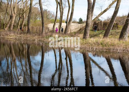 Knokke Heist, Flämische Region - Belgien - 04 03 2021 - spiegelte Bäume in einem Teich mit Besuchern des Naturschutzgebietes im Hintergrund Stockfoto