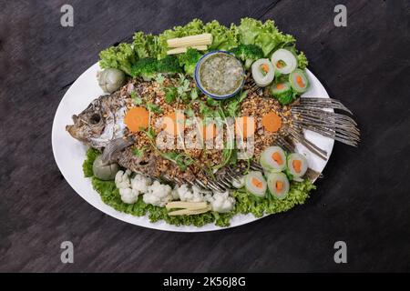 Köstliche frittierte Fisch-Riesengourami Belag mit knusprigem Knoblauch und Kräutersalat mit würzig auf grüner Keramik. Authentisches thailändisches Essen, Draufsicht, selektiv Stockfoto