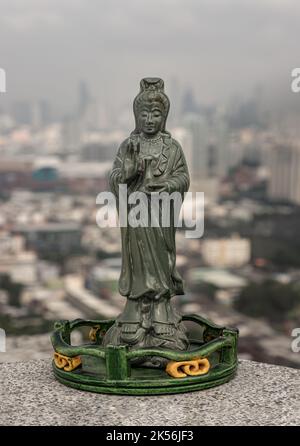 Figur der grünen Guan Yin Bodhisattva oder Quan Yin buddha Statue (Göttin der Barmherzigkeit) mit Blick auf die Stadt im Hintergrund. Platz für Text, selektiver Fokus. Stockfoto