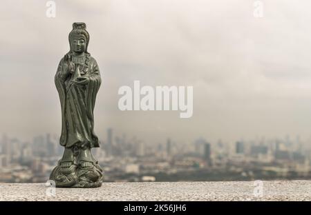 Figur der grünen Guan Yin Bodhisattva oder Quan Yin buddha Statue (Göttin der Barmherzigkeit) mit Blick auf die Stadt im Hintergrund. Platz für Text, selektiver Fokus. Stockfoto