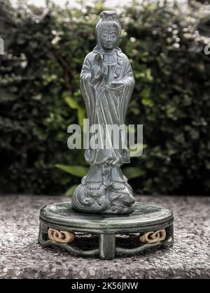 Figur der grünen Guan Yin Bodhisattva oder Quan Yin buddha Statue (Göttin der Barmherzigkeit) mit grünen Blättern Hintergrund. Platz für Text, selektiver Fokus. Stockfoto