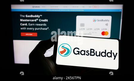 Person, die Mobiltelefon mit dem Logo des US-Kraftstoffpreisunternehmens GasBuddy LLC auf dem Bildschirm vor der Business-Webseite hält. Konzentrieren Sie sich auf die Telefonanzeige. Stockfoto