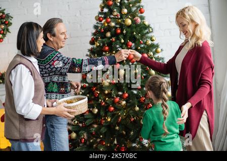 Glückliche blonde Frau Dekoration weihnachtsbaum mit Tochter und multiethnischen Eltern, Stock Bild Stockfoto