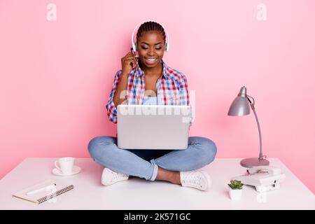 In voller Länge Porträt von attraktiven positiven Mädchen sitzen Schreibtisch kommunizieren Kunden isoliert auf rosa Hintergrund Stockfoto