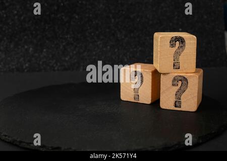 Fragezeichen auf 3 Holzblöcken, isoliert auf dunklem Hintergrund Stockfoto