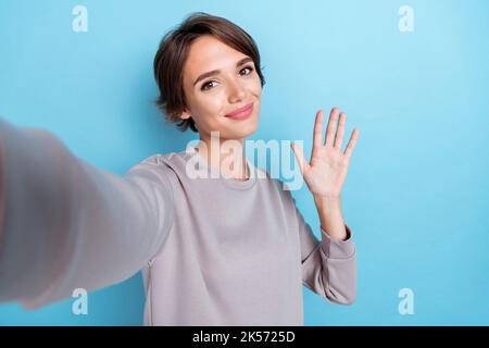 Portrait of adorable niedlichen Mädchen mit bob Frisur tragen grauen Pullover tun Selfie Welle Palme, um Sie isoliert auf blauem Hintergrund Stockfoto