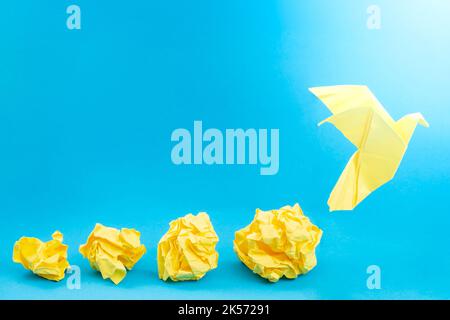 Gelbe zerknitterte Papierkugeln und eine Origami-Taube auf blauem Hintergrund Stockfoto