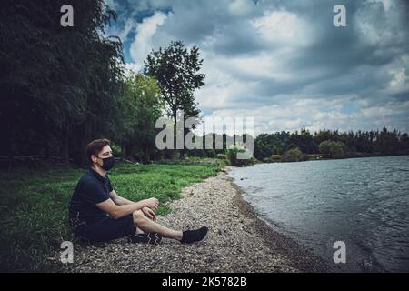 Maskierter Kerl sitzt und schaut auf den See Stockfoto