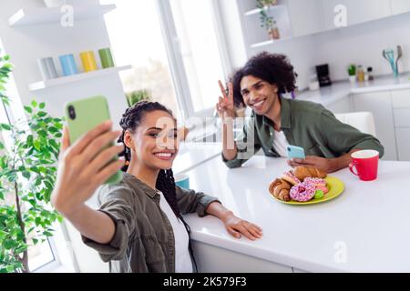 Foto von guten Laune Bruder und Schwester machen Selfie zusammen essen lecker Donuts und trinken Cappuccino Stockfoto