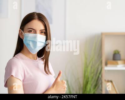 Pandemieschutz. Weibliche Patientin. Impfergebnis. Zufriedene Frau Medizin Maske nach der Injektion zeigt sich wie in hellen Krankenhausraum Innenraum. Stockfoto