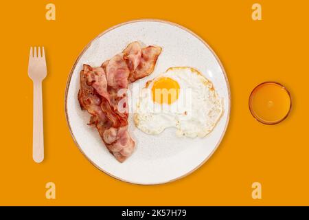 Das beste Frühstück. Speck, ein Spiegelei und Orangensaft. Foto auf einem Sommer gelben Hintergrund. Für Text platzieren. Marketing- und Werbeidee. Modern Stockfoto
