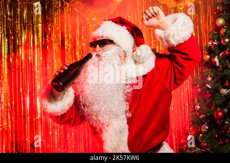 weihnachtsmann in Sonnenbrille mit Champagner-Flasche in der Nähe von weihnachtsbaum und Lametta, Stockbild Stockfoto