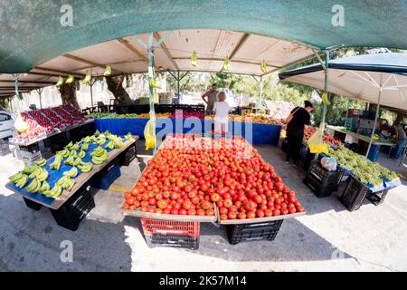 Frisches Obst und Gemüse, einschließlich einer großen Präsentation von Tomaten, die auf einem Marktstand auf einem Freiluftmarkt verkauft werden. Kunden wählen Produkte aus. Stockfoto
