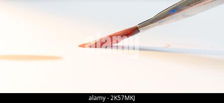 Farblebensdauer. Kunstprozess. Kreative Idee. Finde Inspiration. Pinsel mit leuchtend rot-orangefarbener Farbe, bereit zum Malen auf weißem Papier, Kopierraum. Stockfoto