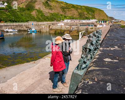 Seniorehepaar mit Blick auf eine Bronzeskulptur zur Erinnerung an die Fischkatastrophe von 1881, Burnmouth Harbour, Berwickshire, Schottland, Großbritannien Stockfoto