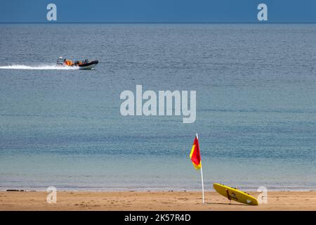 Touristen in einem starren Schlauchboot bei Sommerwetter, in der Nähe des Strandes mit Rettungsschwimmerflagge Coldingham Bay, Berwickshire, Schottland, Großbritannien Stockfoto