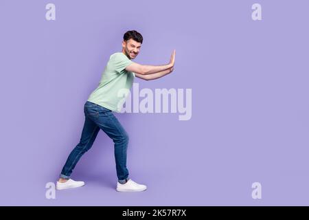 Ganzkörper-Foto von attraktiven jungen Kerl schieben hart Copyspace schwierig tragen trendy graue Kleidung auf violettem Hintergrund isoliert Stockfoto