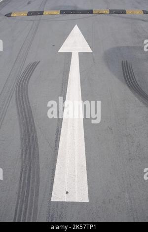 Weißer Pfeil auf der Straße mit Rutschmarken und einem gelb abgestreiften Geschwindigkeitsraub Stockfoto