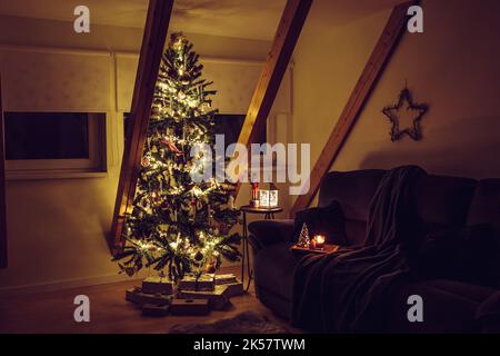 Minimalistisches Wohnzimmer am Heiligabend. Geschmückter Weihnachtsbaum in der Ecke mit beleuchteten Lichtern, Sofa, Tablett mit Kerzen und Sternform. Stockfoto