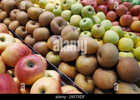 Nahaufnahme von fünf Apfelsorten, die nebeneinander auf einem Marktstand gestapelt sind. Stockfoto