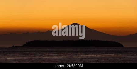 Hinter Mount Baker und Patos Island, von Saturna Island in British Columbia, Kanada aus gesehen, erleuchtete sich ein Morgenhimmel. Stockfoto