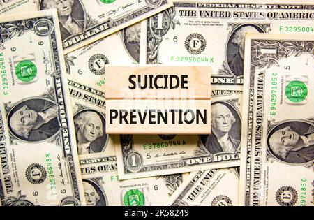 Symbol für die Suizidprävention. Konzept Wörter Selbstmordprävention auf Holzblöcken. Schöner Hintergrund von Dollarscheinen. Dollarscheine. Psychologische und Stockfoto