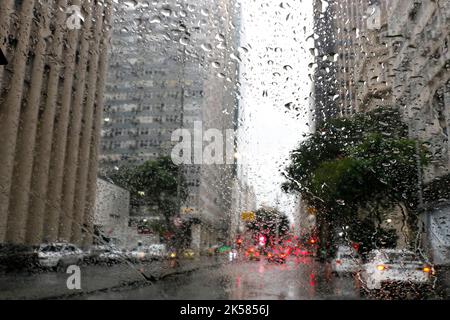 Regen fällt auf das Autofenster. Kaltes Wetter Regenzeit, bewölkt, nasser Tag. Einsame Stimmung. Stadt verschwommen Hintergrund. Fahrersicht. Stockfoto