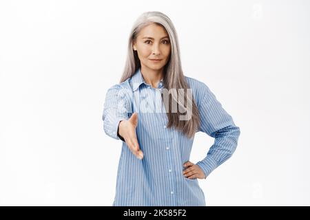 Bild einer lächelnden asiatischen älteren Frau, die Sie mit den Händen schüttelt, grüßt, über dem weißen Studiohintergrund steht Stockfoto