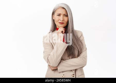 Besorgte asiatische Geschäftsfrau, ältere Geschäftsfrau, die mit unruhigen Gesichtsausdrücken zuhört und auf weißem Hintergrund steht Stockfoto