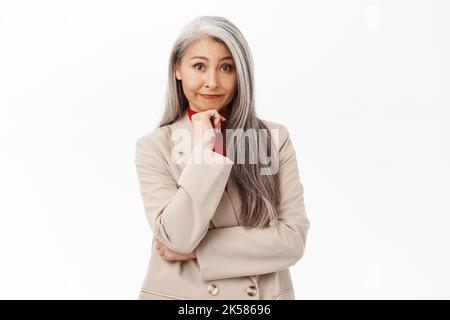 Porträt einer koreanischen Geschäftsfrau, Frau mit grauen Haaren denkend, Anzug, lächelnd fasziniert, stehend auf weißem Hintergrund Stockfoto