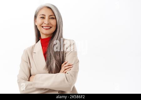 Porträt einer erfolgreichen asiatischen Geschäftsfrau, lächelnd und glücklich aussehend, professionelle Power Pose, Corporate Outfit, stehend über weiß Stockfoto