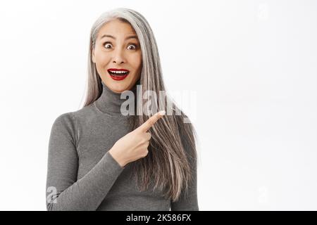 Porträt einer schönen koreanischen Frau mittleren Alters, die glücklich und lächelnd aussieht, mit dem Finger auf die rechte obere Seite zeigt, Banner oder Logo, Werbung Stockfoto