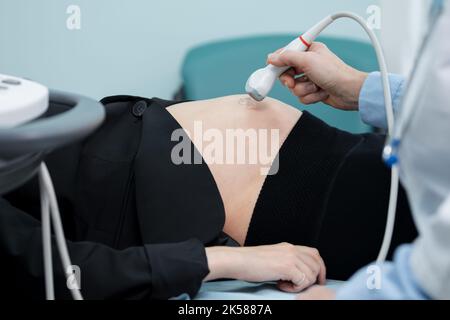 Die Hand schiebt den Schallkopf über den Abdomen und überprüft die Anzeichen eines Gestrüchs Stockfoto