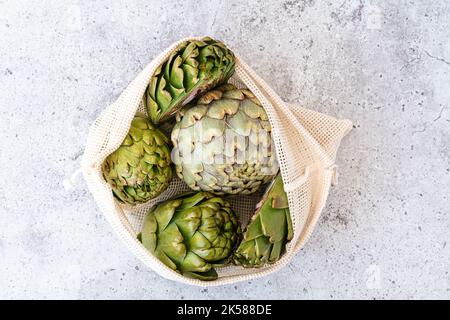 Draufsicht auf Artischocke in Leinenbeutel auf dem Tisch. Flaches Lay von gesunden Lebensmitteln Gemüse. Stockfoto