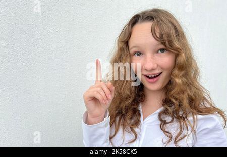 Ein Mädchen auf weißem Hintergrund in einer weißen Bluse, hellhaarig, zeigt andere fröhliche Emotionen, sie macht Gesichter, sie lacht fröhlich, sie kräuselt ihre Haare und zeigt ihre Zunge. Hochwertige Fotos Stockfoto