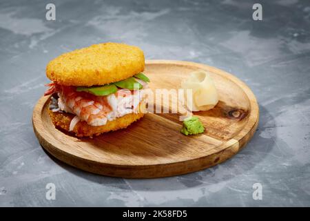 Konzept der panasiatischen Küche. Japanischer Sushi-Burger aus Reisbrot, Krabbenfleisch, Avokado und Wasabi-Sauce. Servieren auf Holzbrett. Platz kopieren Stockfoto