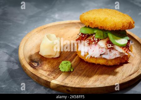 Konzept der panasiatischen Küche. Japanischer Sushi-Burger aus Reisbrot, Krabbenfleisch, Avokado und Wasabi-Sauce. Servieren auf Holzbrett. Platz kopieren Stockfoto