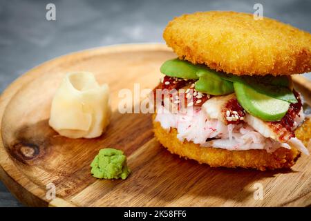 Konzept der panasiatischen Küche. Japanischer Sushi-Burger aus Reisbrot, Krabbenfleisch, Avokado und Wasabi-Sauce. Servieren auf Holzbrett. Platz kopieren Stockfoto