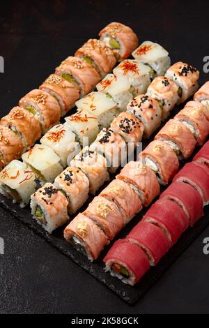 Draufsicht Hintergrund mit einer Reihe von bunten verschiedenen Arten von Sushi-Rollen auf schwarzem Hintergrund platziert Stockfoto