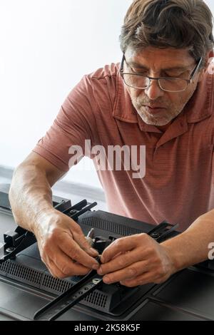 lateinischer Mann, der eine Basis für den Fernseher stellt, damit er an der Wand befestigt werden kann Stockfoto