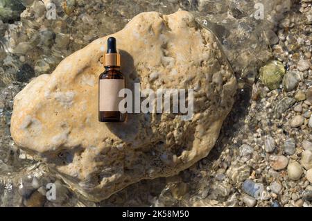 Fläschchen-Serum, kosmetisch in klarem, transparentem Wasser auf Stein, flach liegend, Draufsicht, Kopierraum. Leeres Etikett, Modell. Natürlicher Hintergrund, Steine und Wasser Stockfoto