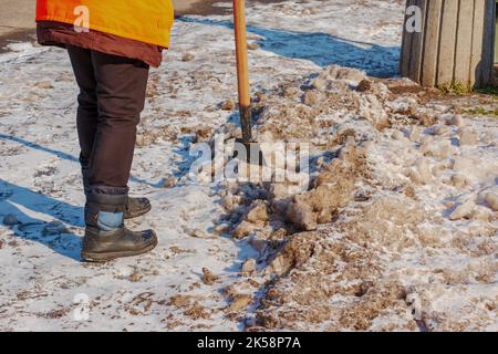 Eine Arbeiterin reinigt das Eis und entfernt mit einem Eisbrecher Schnee von den Pflasterplatten. Ein Mann bricht Eis mit einem Stahlklingenbrecher, ein Eisbrecher ebenfalls Stockfoto