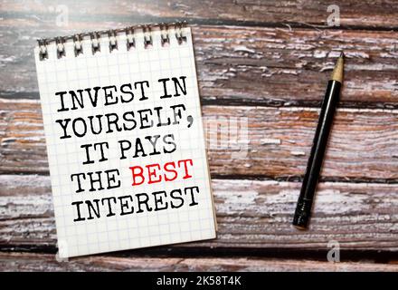 Text Invest in Yourself Es zahlt das beste Interesse geschrieben in Notizblock, Office Holz Tabelle von oben, Konzept Bild für Blog-Titel oder Header-Bild. Gealtert Stockfoto