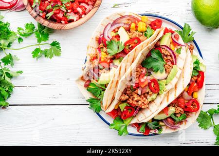 Mexikanische Küche. Tacos mit Rindfleisch, Mais, roten Bohnen, Tomatensalsa-Sauce und Zwiebeln in Mais-Tortilla auf dem Teller. Weißer Tischhintergrund, Draufsicht Stockfoto